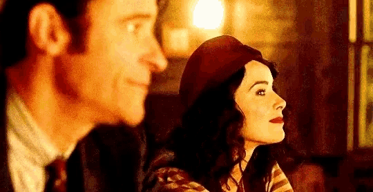 a man and a woman are looking at each other . the woman is wearing a red hat .