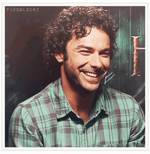 a man with curly hair is smiling in front of a sign that says piedalecki