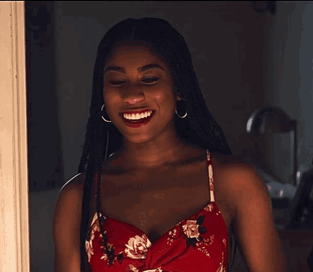 a woman wearing a red floral dress and hoop earrings smiles