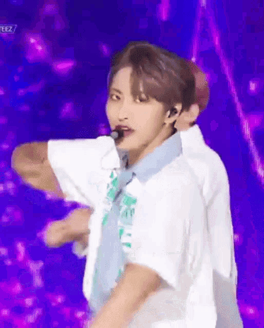 a man in a white shirt and blue tie is dancing on a stage with a microphone in his mouth .