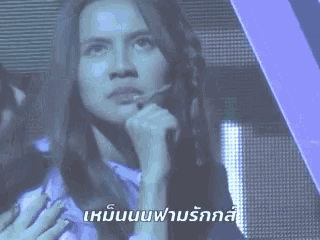 a woman is sitting in front of a microphone with a foreign language written on the screen behind her