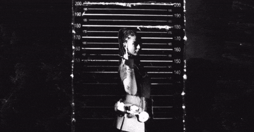 a black and white photo of a woman standing in front of a ruler with numbers from 100 to 200 on it