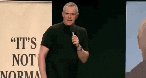 a man is standing in front of a microphone in front of a sign that says `` it 's not norma '' .