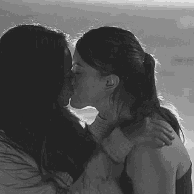 a couple of women kissing on the beach in a black and white photo