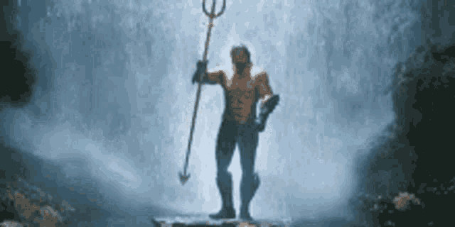 a man in a superhero costume is holding a trident in front of a waterfall .