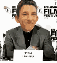 a man sitting at a table with a sign that says tom hanks on it