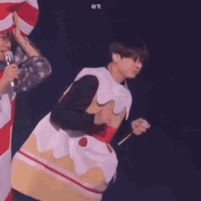 a man in a cake costume is holding a fork and smiling on a stage .