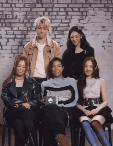 a group of people sitting in front of a brick wall with a man wearing a sweater with the letter o on it