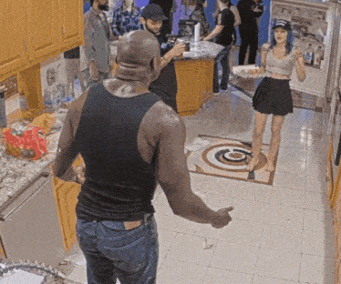 a man in a black tank top stands in a kitchen