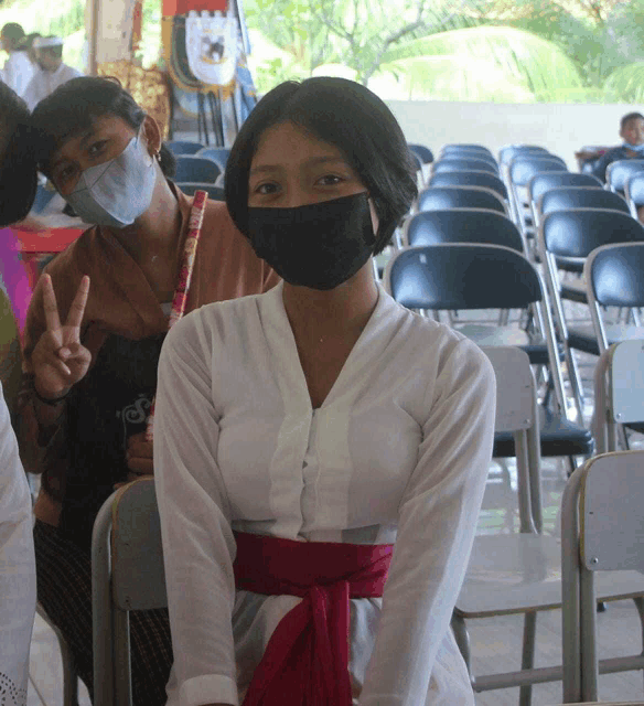 a woman wearing a black face mask sits in a row of chairs