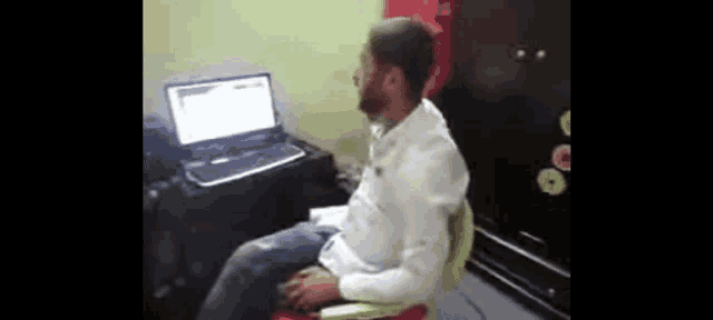 a man is sitting in a chair in front of a laptop .