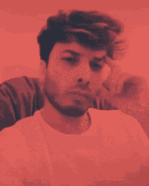 a man in a white t-shirt has his hand on his chin in a red background