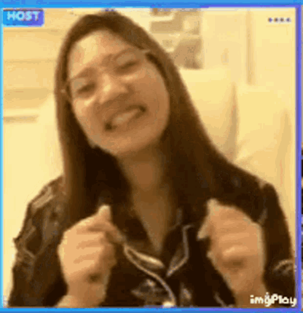 a woman wearing glasses is smiling and making a funny face while sitting on a couch .