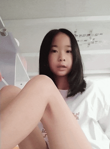 a girl wearing a white shirt that says ' s ' on it sits on a bed