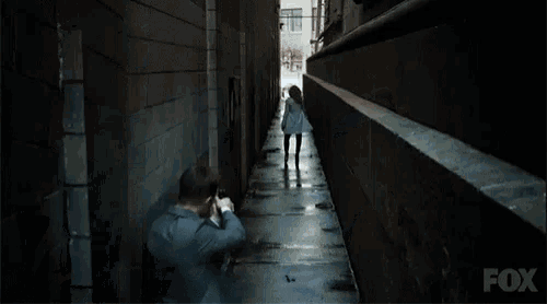 a man in a suit is holding a gun in front of a brick wall with fox written on it