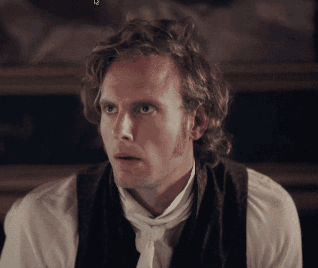 a man with curly hair wearing a white shirt and a brown vest