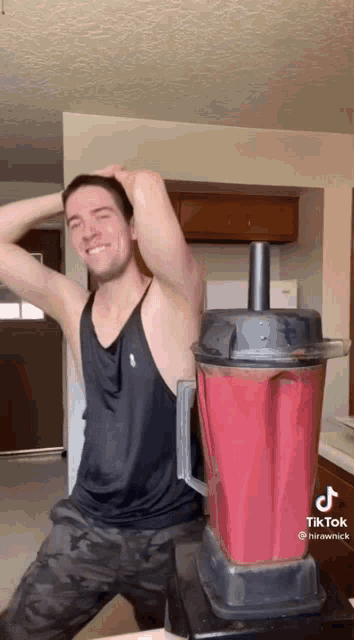 a man in a black tank top is standing next to a blender .