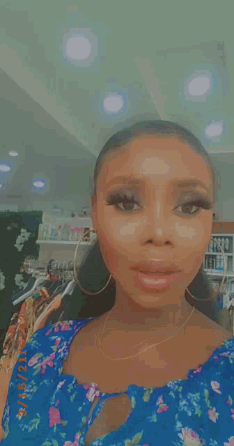 a woman wearing a blue floral dress and gold hoop earrings is taking a selfie .
