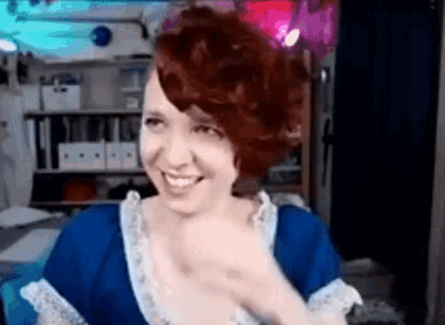 a woman with red hair is smiling while wearing a blue dress and white lace trim .