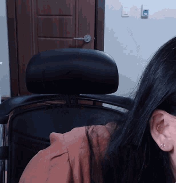 a woman with long black hair sits in a chair in front of a door
