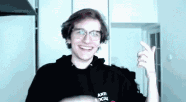 a man wearing glasses and an anti social social club hoodie is smiling and pointing at the camera .