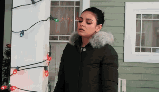 a woman in a black jacket is standing in front of a house with christmas lights on it