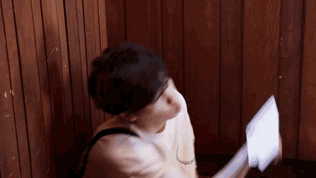 a person standing in front of a wooden wall holding a piece of paper in their hand