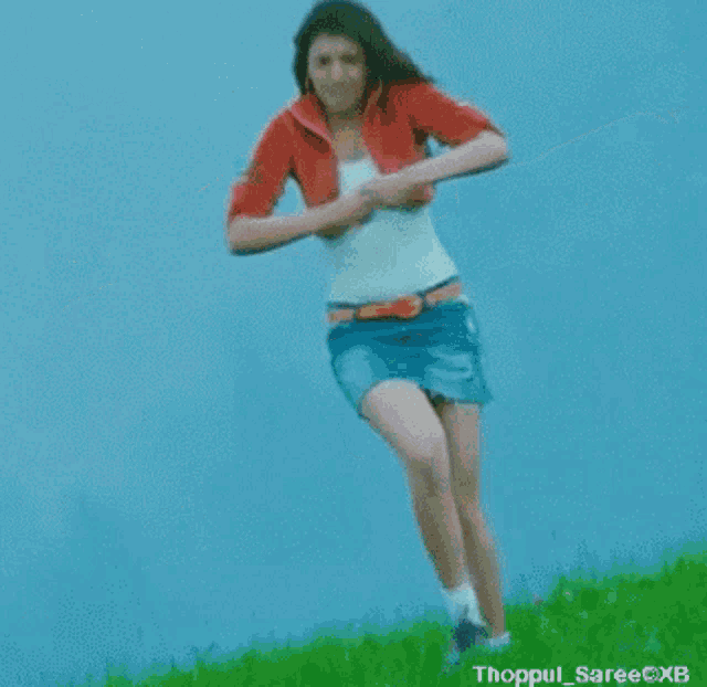 a woman in a denim skirt and a white tank top is standing on top of a grassy hill with her arms wide open .