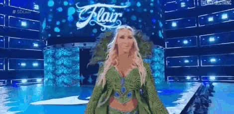 a woman in a green dress is walking on a stage in front of a sign that says ' flair ' on it .
