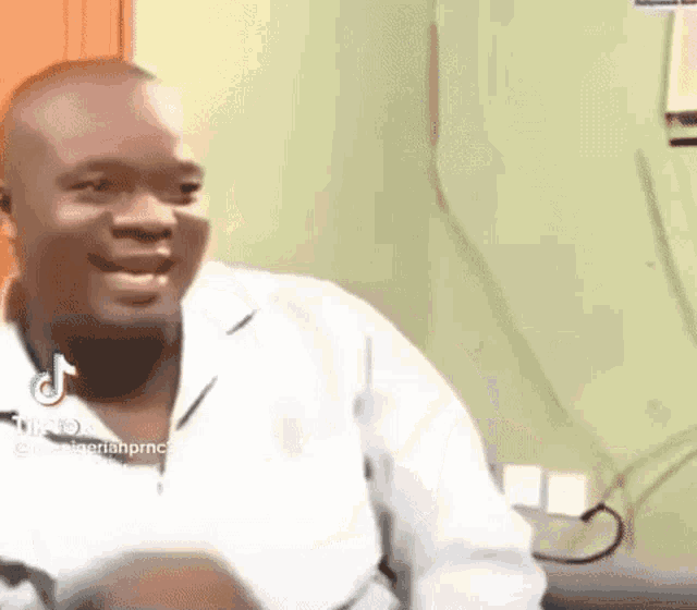 a man in a white shirt is sitting in a chair and smiling .