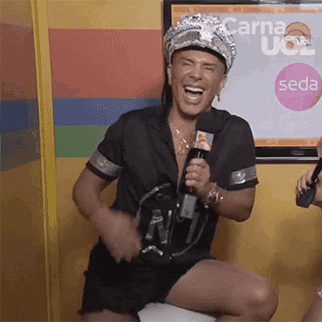 a man is holding a microphone and laughing in front of a screen that says seda