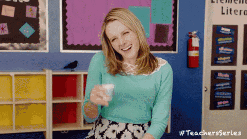 a woman in a blue shirt is smiling in a classroom with a fire extinguisher hanging on the wall