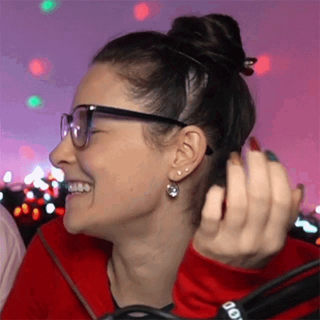 a woman wearing glasses and earrings is smiling and holding her hair in a bun .