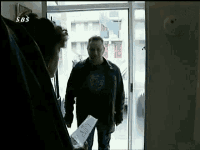a man in a black shirt is standing in a doorway with a sbs logo on the corner