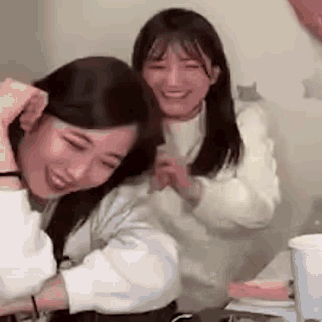 two women are hugging each other and smiling while sitting next to each other in a room .