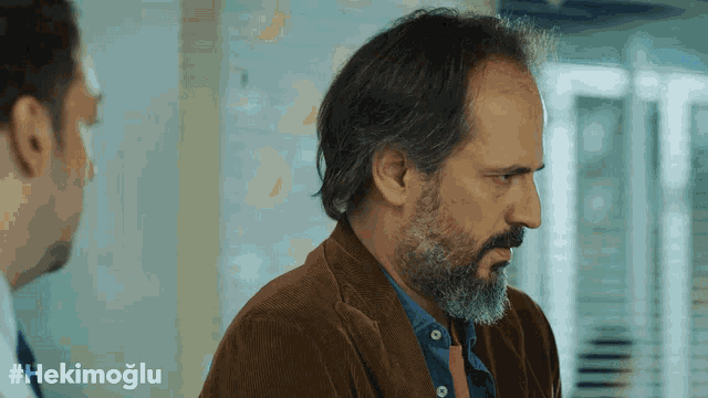 a man with a beard is standing next to another man with #hekimoglu written on the bottom