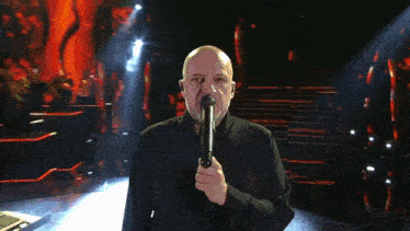 a bald man singing into a microphone with the number 5 in the back