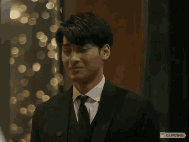 a man in a suit and tie is smiling in front of a wall with lights on it