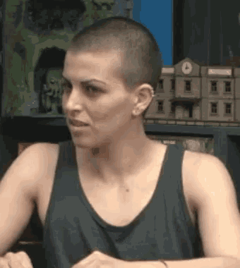 a woman with a shaved head is wearing a black tank top and earring .