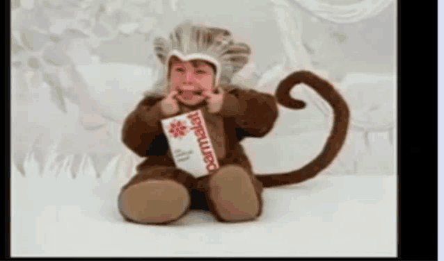 a baby dressed in a monkey costume holds a carton of parmalat toothpaste