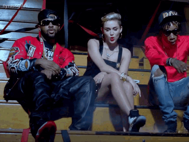 a man in a red jacket with the word raw on it sits next to a woman sitting on a bench