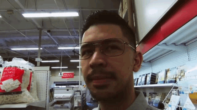 a man wearing glasses is standing in front of a bag of microwave popcorn