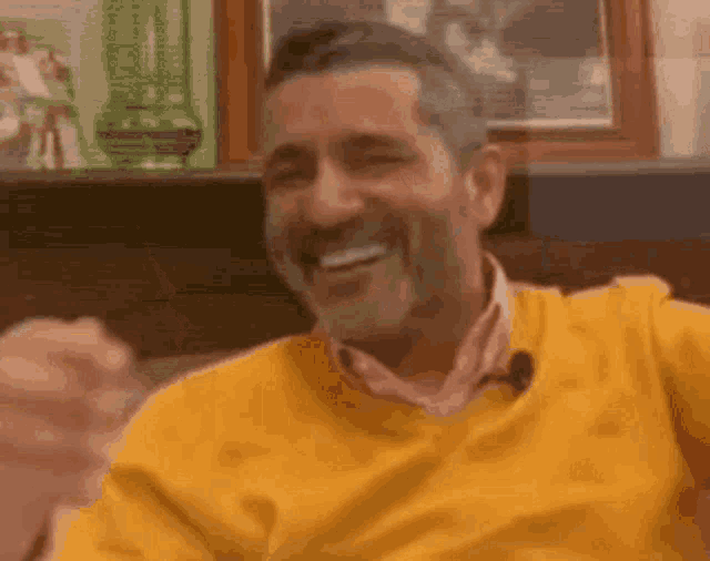 a man wearing a yellow sweater and a pink shirt is laughing while sitting on a couch .