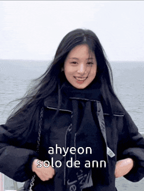 a woman in a black jacket and scarf is standing in front of the ocean .