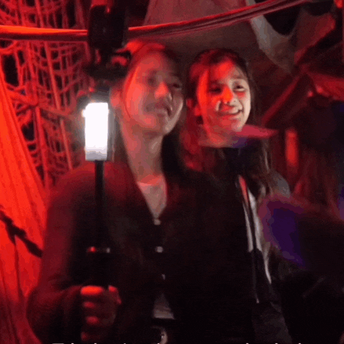 two girls are posing for a picture in a dark room with a red light behind them