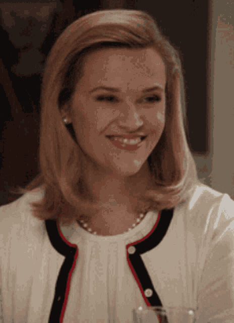 a woman wearing pearls and a white shirt smiles