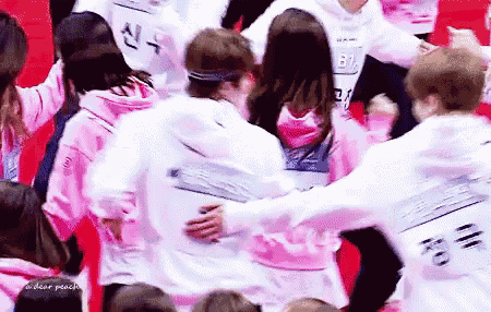 a group of people are hugging each other in a crowd while wearing pink sweatshirts .