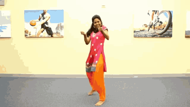 a woman in a pink dress and orange pants is dancing in a room