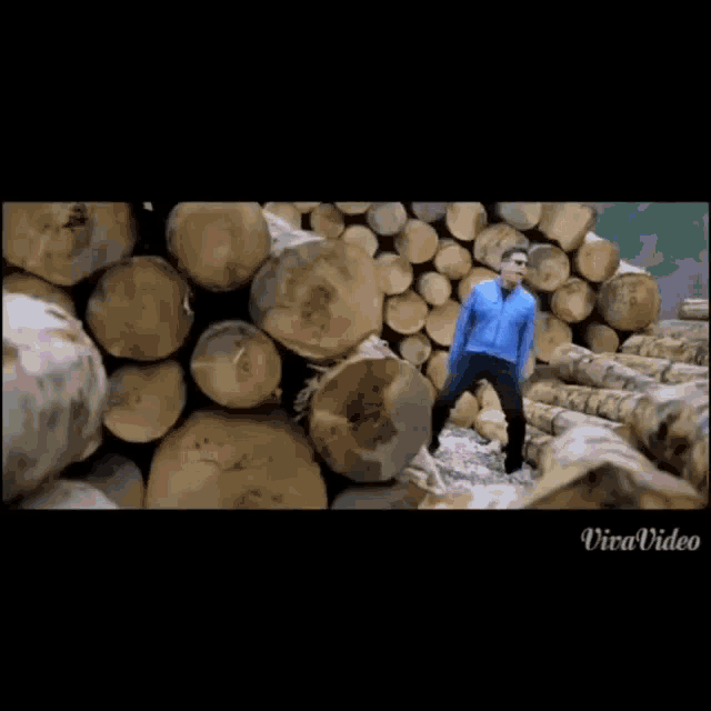 a man in a blue jacket is dancing in front of a pile of logs