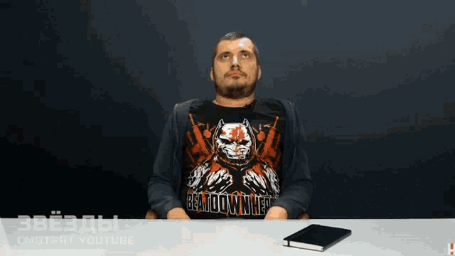 a man sitting at a table wearing a black shirt that says beat down white